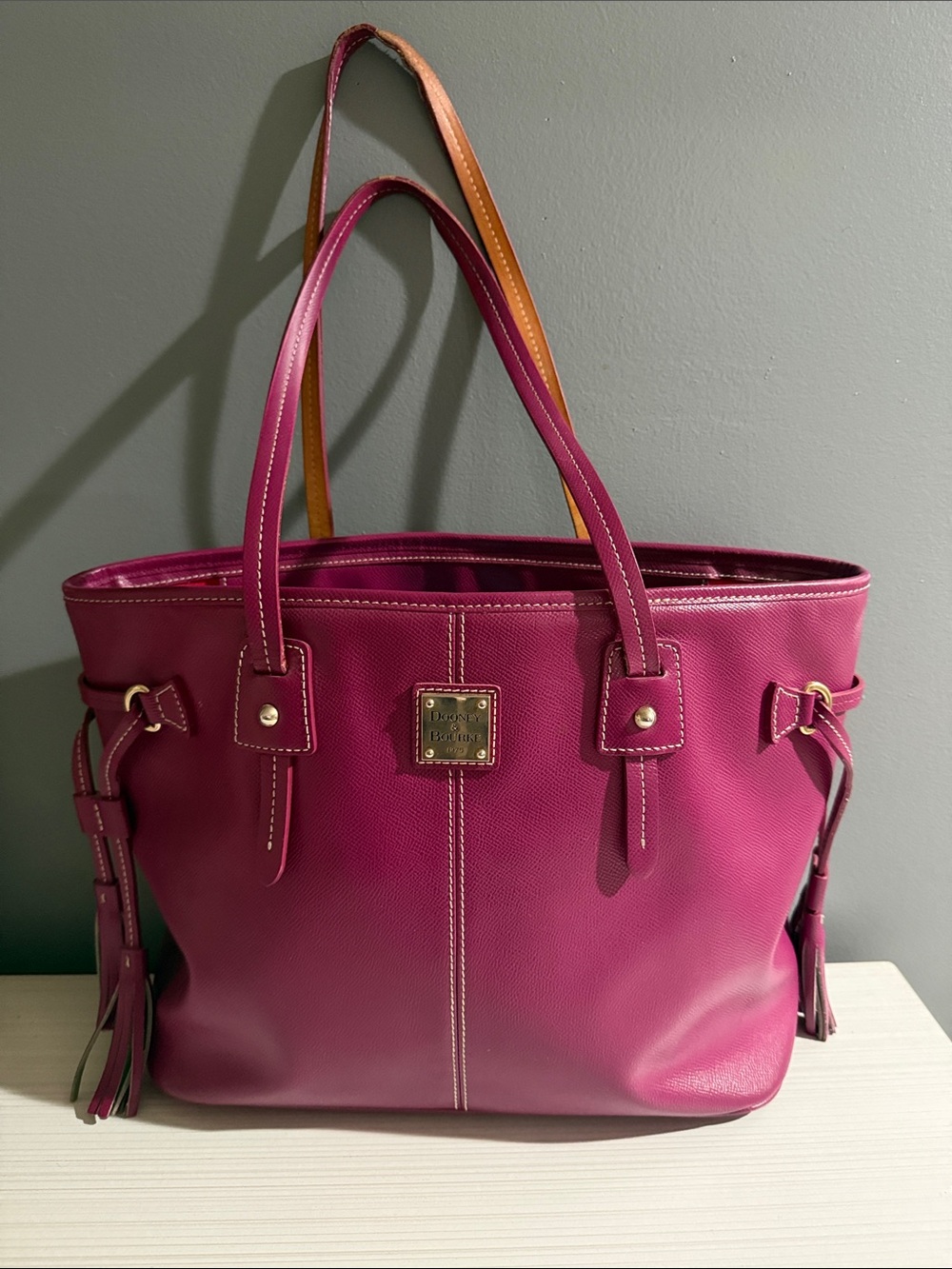 Dooney & Bourke contrasting tan handles, gold-tone hardware, and side tassels.